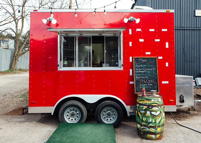 a small red food truck with a barrel infront of it