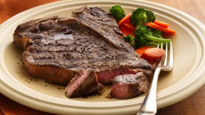 cooked red meat on a plate next to some salad