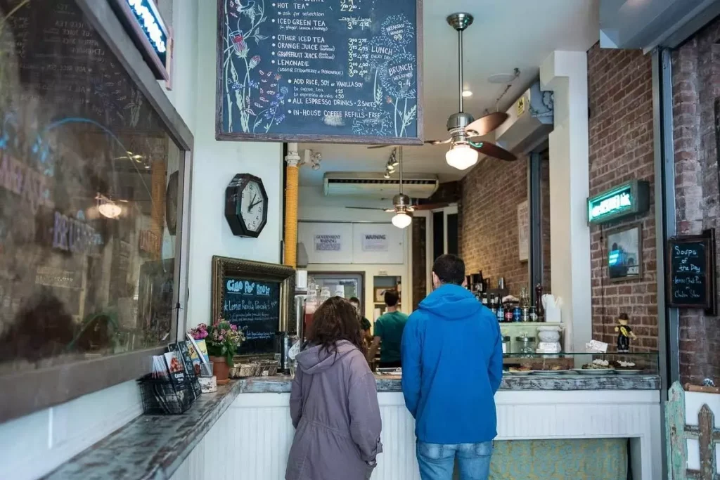 a guy in a blue hoodie and a girl in a purple hoode ordering coffee in a shop