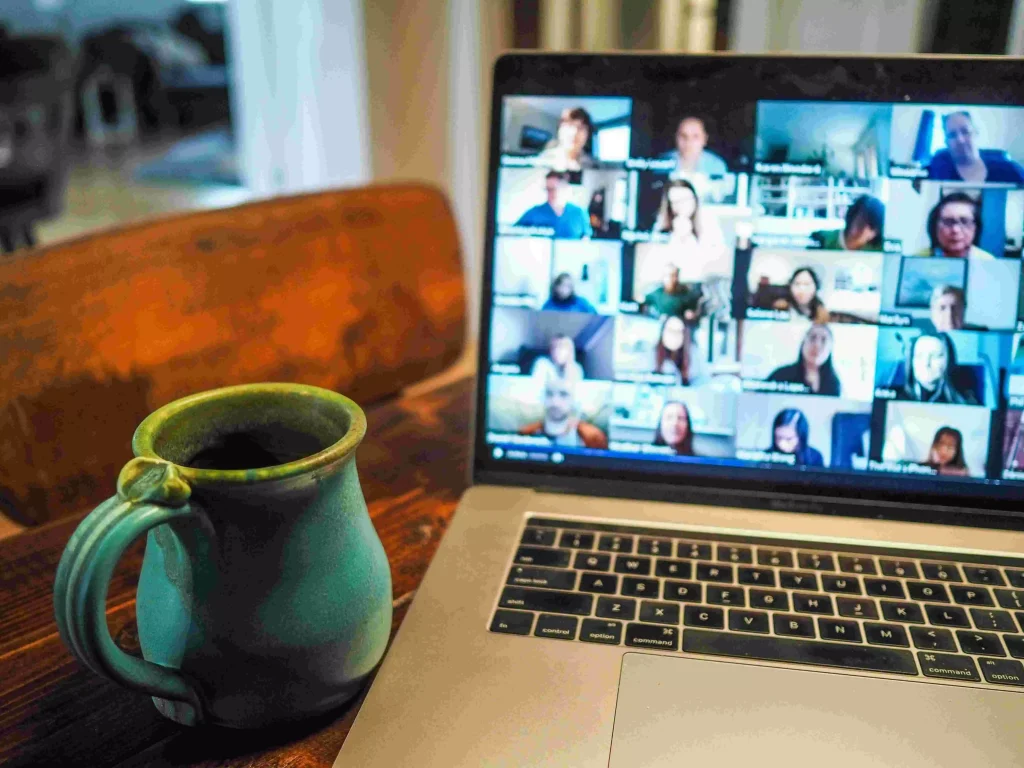 a laptop with an opened video call and a green cup next to the laptop on an office desk