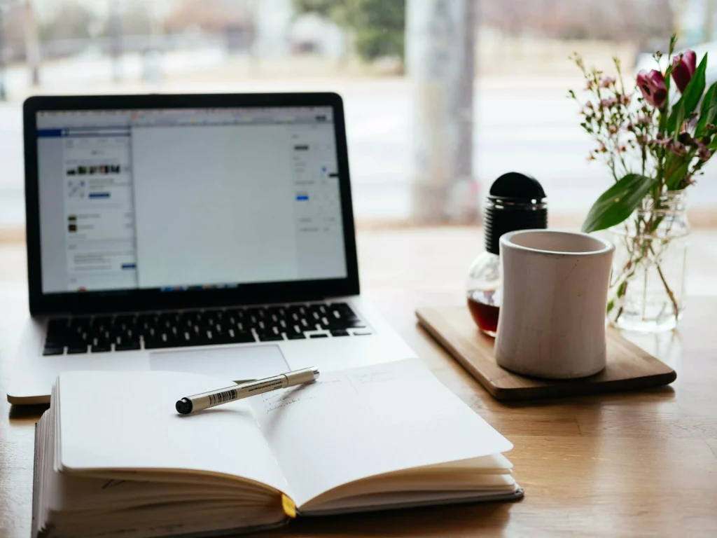 a notebook with blank pages in front of a laptop and a cup of coffe