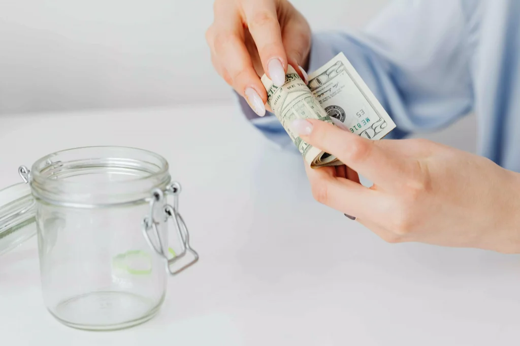 a person holding paper bills next to a glass jar