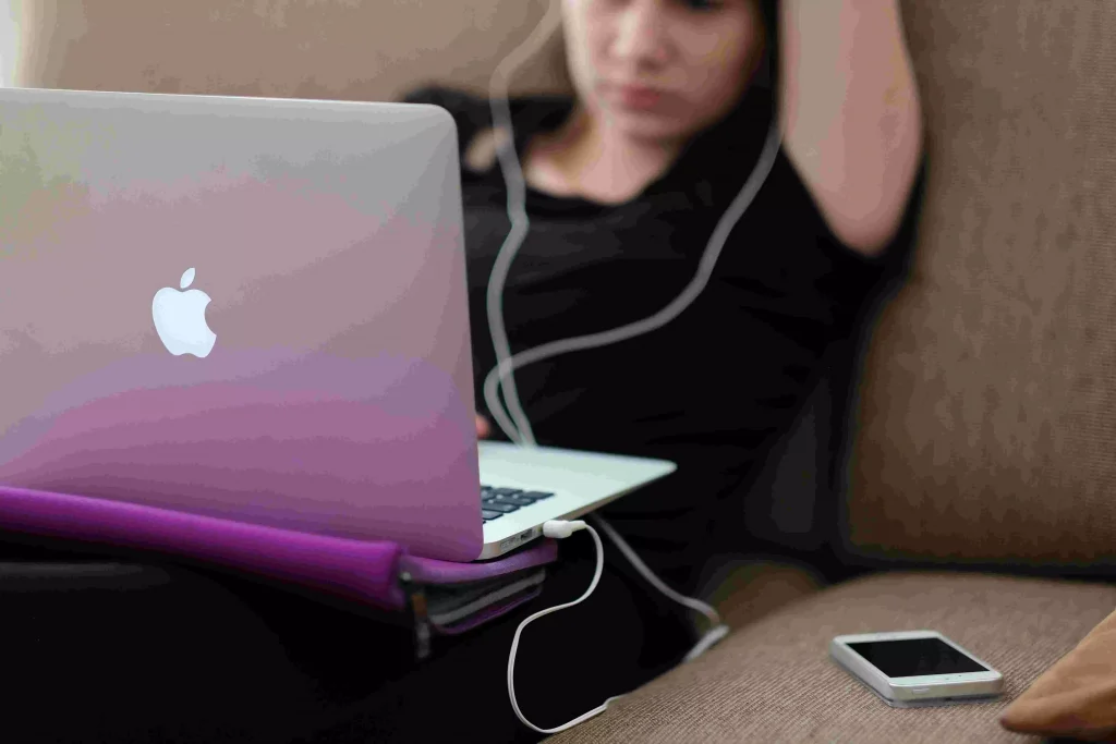 a girl with her headphones looking at a pink laptop