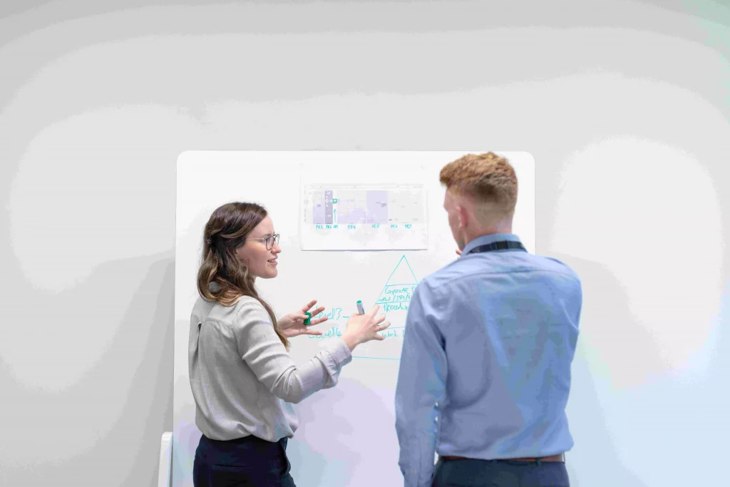 a women showing something on a board to a man in a blue shirt