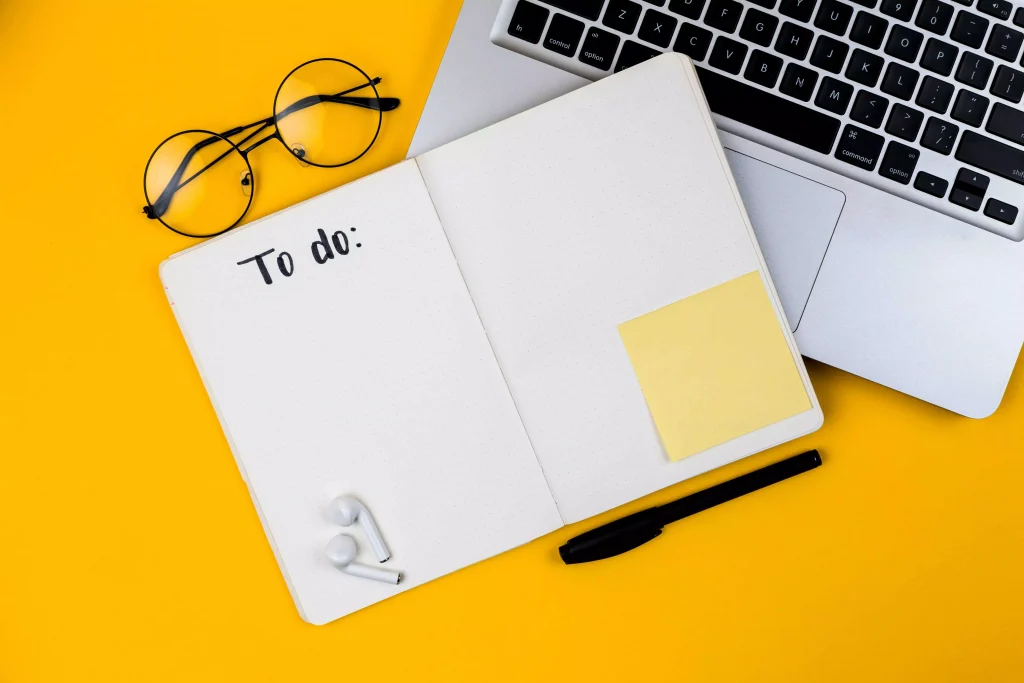 a notebook with a laptop, pen and glasses next to it