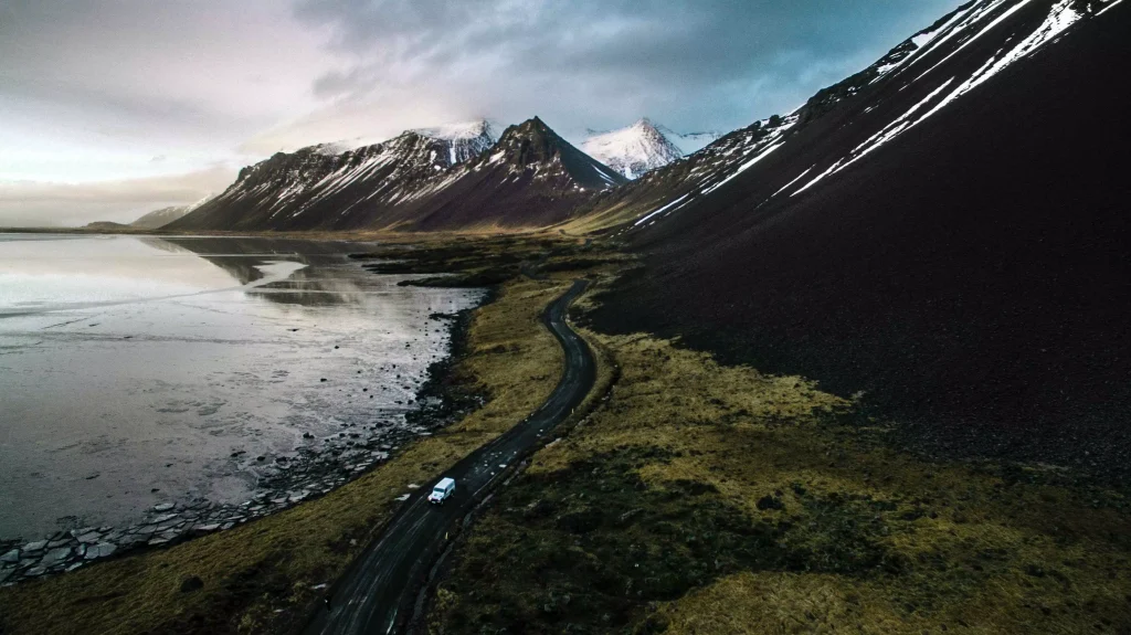 green fields and mountains with snow on top of them next to the ocean