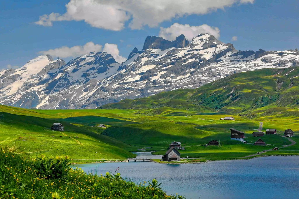 mountains next to a lake and green fields